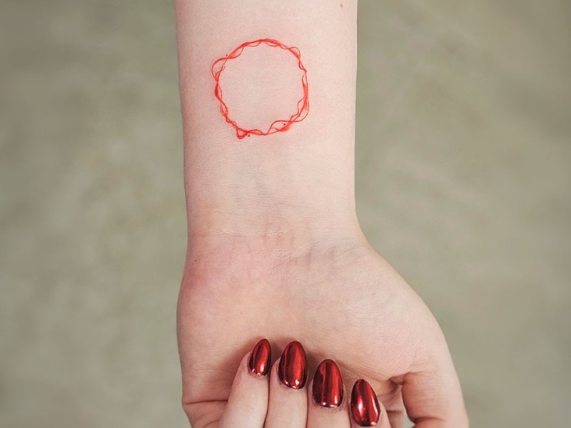 Minimal red ink circle tattoo on the wrist by Klaudia at Silent Moon, our private tattoo studio in Bermondsey, South East London.