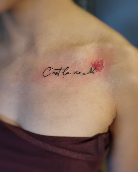 Fine line "C'est la vie" script tattoo with a red flower by Klaudia at Silent Moon, our private tattoo studio in Bermondsey, South East London.