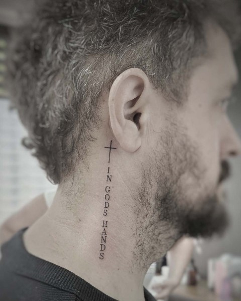 Fine line cross and lettering tattoo behind the ear by Klaudia at Silent Moon, our private tattoo studio in Bermondsey, South East London.