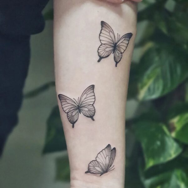 Delicate fine line blackwork tattoo on the forearm/wrist featuring a trio of realistic butterflies in different sizes. Custom minimalist animal piece tattooed at Silent Moon Tattoo Studio in London.