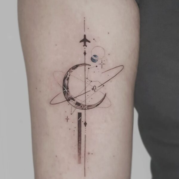 Delicate fine line geometric tattoo on the upper arm featuring a crescent moon, planet orbits, a small airplane silhouette, and star/dotwork accents. Custom celestial travel piece tattooed at Silent Moon Tattoo Studio in London.