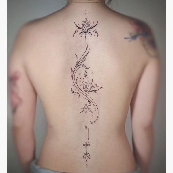 Elegant fine line ornamental tattoo running vertically along the spine, featuring stylized lotus flowers, symmetrical scrollwork, and dotwork accents. Custom spiritual blackwork piece tattooed at Silent Moon Tattoo Studio in London.
