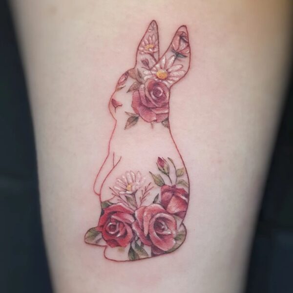 Illustrative colour tattoo on the leg/arm featuring a rabbit silhouette filled with micro realism red roses and daisy flowers. Custom botanical animal piece tattooed at Silent Moon Tattoo Studio in London.