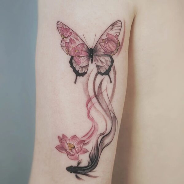 Illustrative colour tattoo on the upper arm featuring a pink-filled butterfly, black Koi fish, pink lotus flower, and abstract smoke/wave elements. Custom symbolic piece tattooed at Silent Moon Tattoo Studio in London.