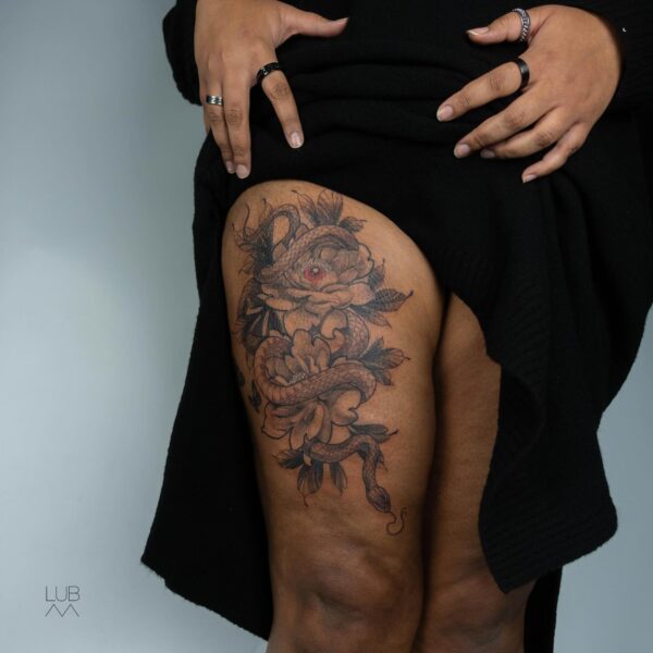 Illustrative black and grey tattoo on the thigh of a snake coiled through peony flowers, with a red color accent in the flower center. Custom botanical art tattooed at Silent Moon Tattoo Studio London UK.