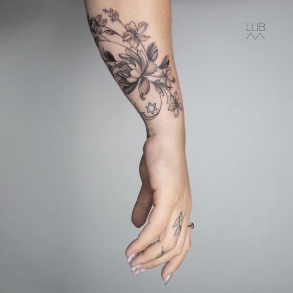 Black and grey fine line floral forearm tattoo with delicate botanical bouquet, soft shading, and a Star of David symbol. Custom meaningful art tattooed at Silent Moon Tattoo Studio London UK.