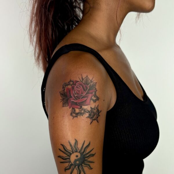 Red rose tattoo with thorns on upper arm by tattoo artist at Silent Moon Tattoo Studio in London.