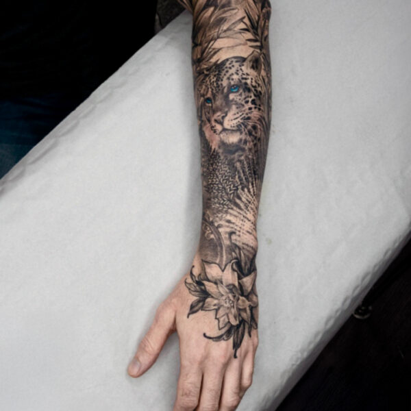 Realistic leopard tattoo sleeve with floral and leaf design by tattoo artist at Silent Moon Tattoo Studio in London.