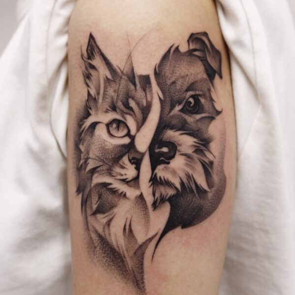 Black and grey realism portrait tattoo blending half a cat face and half a dog face on the upper arm. Custom pet portrait tattooed at Silent Moon Tattoo Studio London UK.