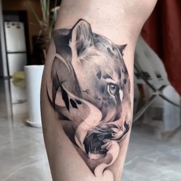 Black and grey realism jaguar portrait tattoo on calf with abstract smoke and graphic line work. Custom wildlife art tattooed at Silent Moon Tattoo Studio London UK.