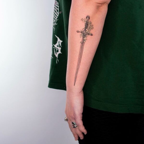 Fine line sword tattoo with ivy leaves on forearm by tattoo artist at Silent Moon Tattoo Studio in London