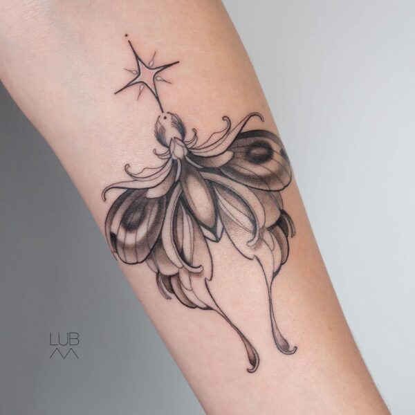 Illustrative black and grey moth tattoo on the forearm with delicate wings, fine line detail, and a shining star motif. Custom blackwork and celestial design tattooed at Silent Moon Tattoo Studio in London.