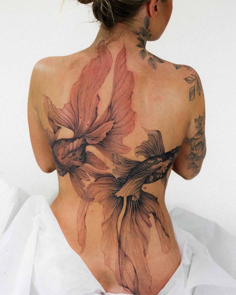 Fine line illustrative back piece of two betta fish with long, flowing fins in soft red and black linework, covering the full back, by Dominika.